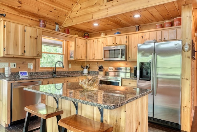 kitchen featuring light brown cabinets, dark wood-style floors, dark stone counters, a sink, and appliances with stainless steel finishes