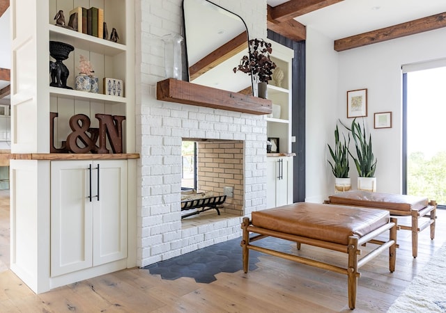 living room with beam ceiling, a healthy amount of sunlight, built in shelves, and light wood-type flooring