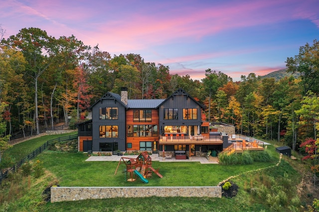 back house at dusk with a deck, a patio, and a yard