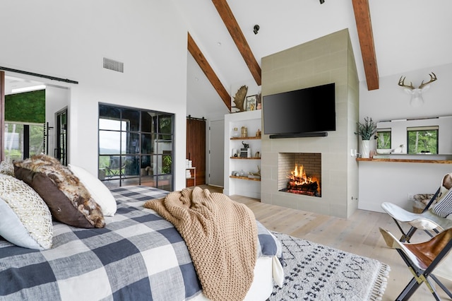 bedroom with multiple windows, a fireplace, light hardwood / wood-style flooring, and beamed ceiling