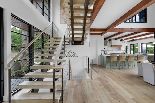 staircase with beamed ceiling, wood-type flooring, and a high ceiling