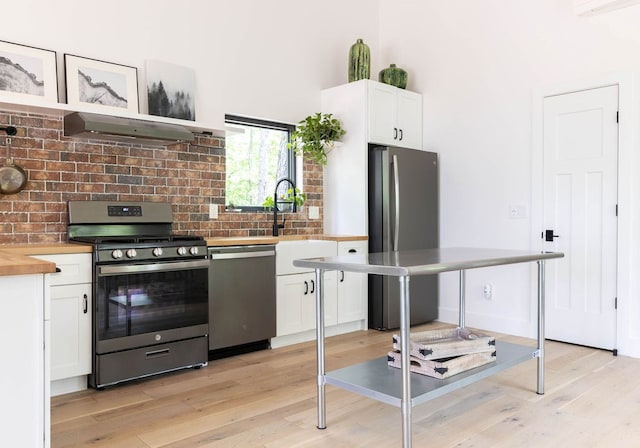 kitchen with appliances with stainless steel finishes, light hardwood / wood-style flooring, butcher block countertops, wall chimney range hood, and white cabinets