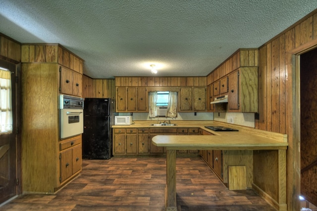 kitchen featuring under cabinet range hood, light countertops, brown cabinets, dark wood-style floors, and black appliances