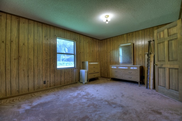 unfurnished bedroom featuring wooden walls, radiator heating unit, a textured ceiling, and carpet flooring