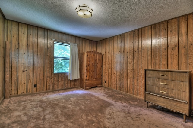 spare room with carpet floors, a textured ceiling, and wooden walls