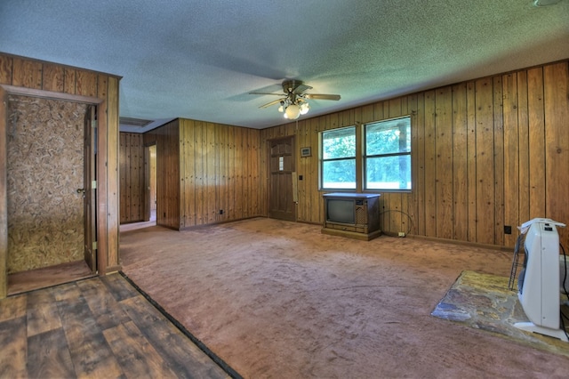 carpeted spare room featuring a textured ceiling, ceiling fan, and wooden walls