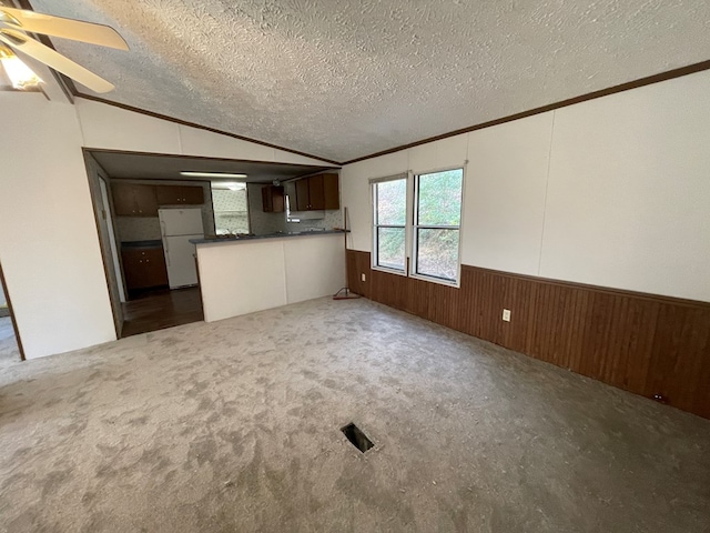 interior space with dark colored carpet, wood walls, vaulted ceiling, a textured ceiling, and white fridge