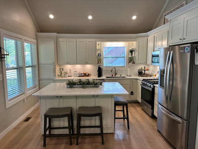 610 E Second St, Blue Ridge, GA 30513 - kitchen featuring appliances with stainless steel finishes, vaulted ceiling, wood finished floors, a kitchen breakfast bar, and tasteful backsplash