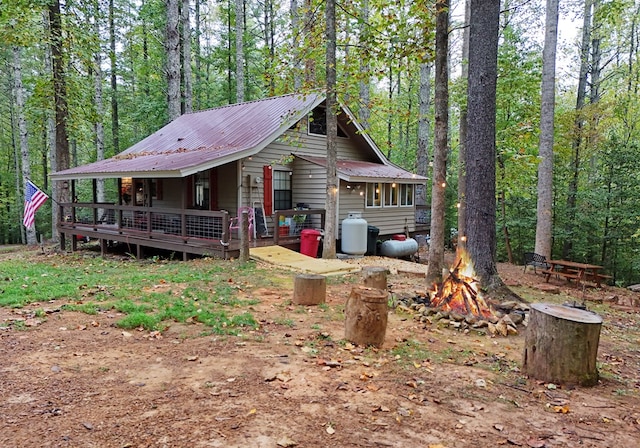 view of front of house featuring metal roof, a view of trees, a fire pit, and a deck