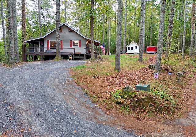 rustic home with dirt driveway, a view of trees, and a deck