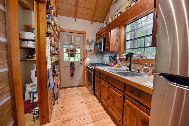 kitchen featuring light wood finished floors, wood ceiling, a sink, decorative backsplash, and appliances with stainless steel finishes