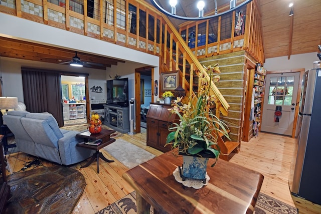 living room featuring light wood finished floors, stairs, a towering ceiling, a fireplace, and beam ceiling