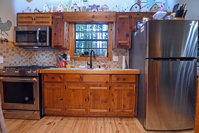 kitchen with light countertops, appliances with stainless steel finishes, brown cabinetry, and a sink