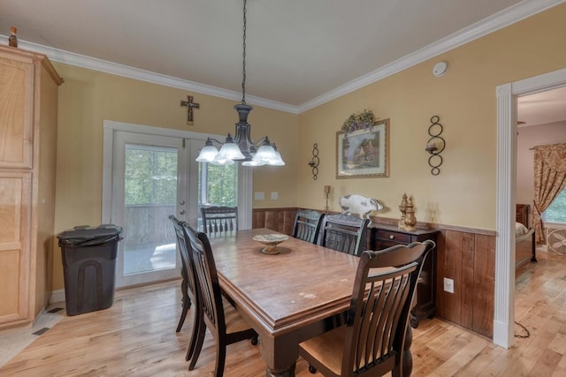 dining room featuring crown molding, wood walls, french doors, and light wood-type flooring