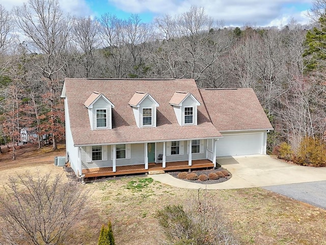 cape cod home with a front yard, covered porch, a view of trees, a garage, and driveway