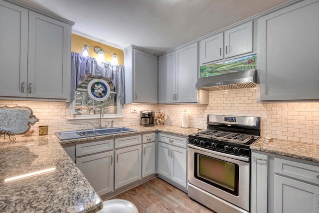 kitchen featuring gas range, light stone countertops, premium range hood, light hardwood / wood-style floors, and decorative backsplash