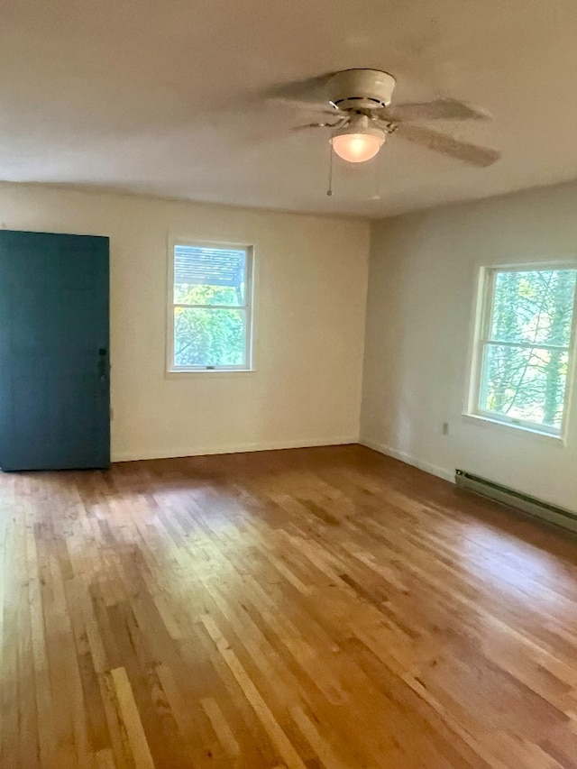 spare room featuring light wood-type flooring, baseboard heating, ceiling fan, and a wealth of natural light