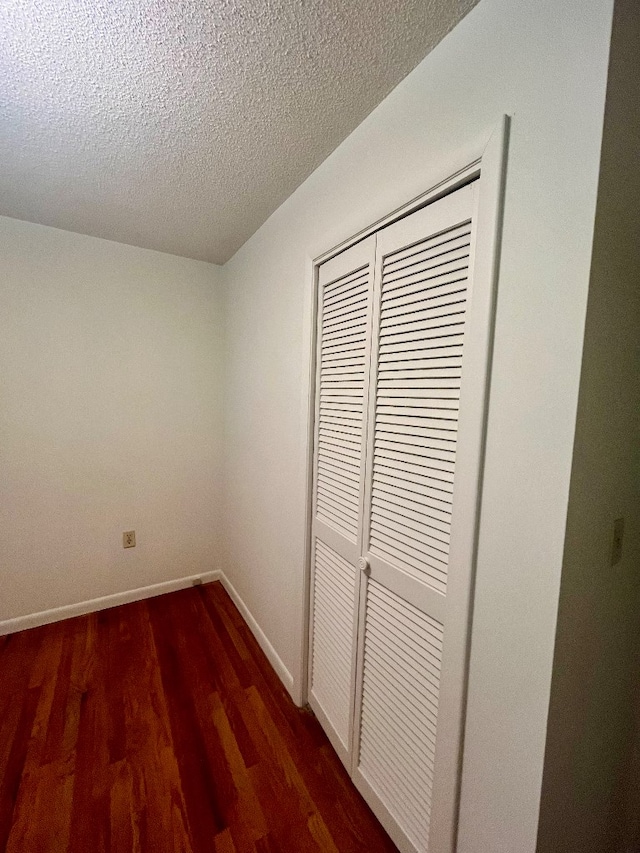 unfurnished bedroom with a textured ceiling, dark hardwood / wood-style floors, and a closet