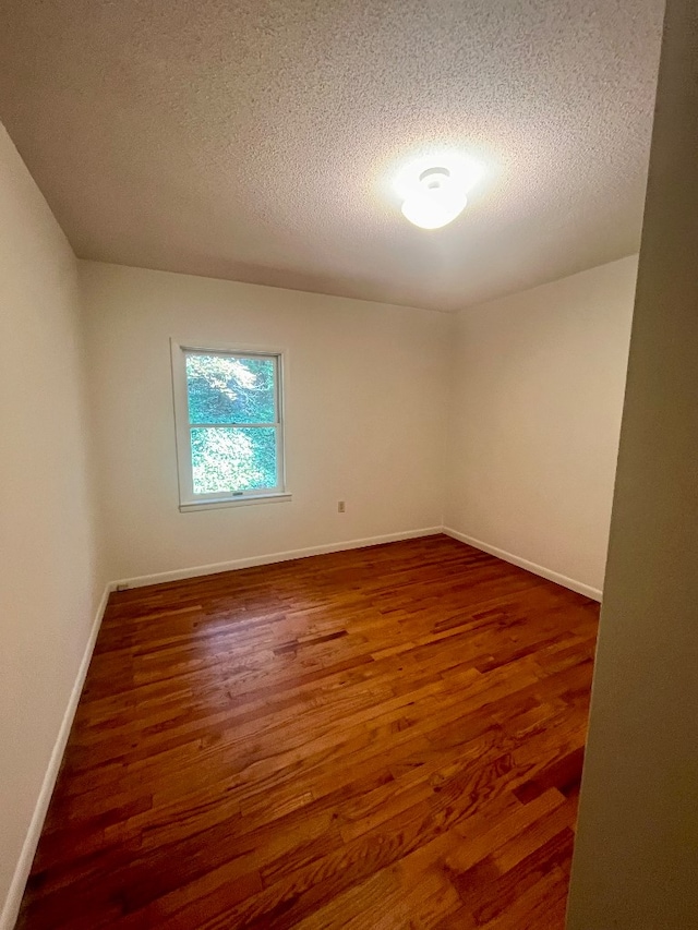 empty room with a textured ceiling and dark hardwood / wood-style flooring