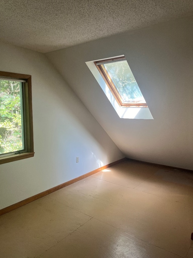 additional living space with a textured ceiling and lofted ceiling with skylight