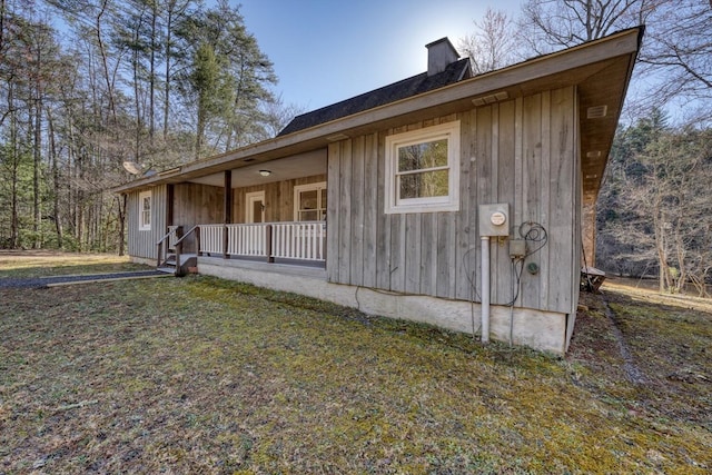 view of side of property featuring a yard, board and batten siding, a porch, and a chimney
