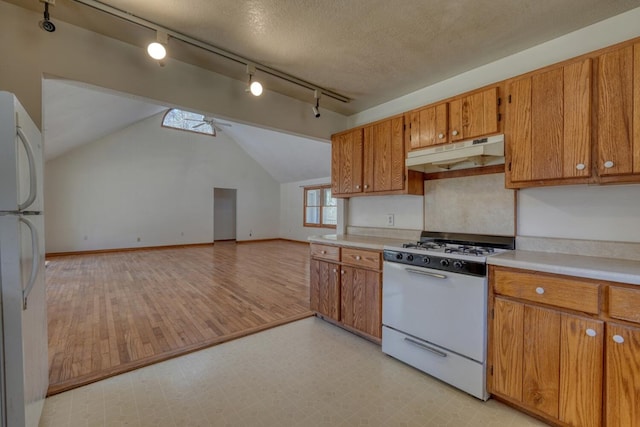 kitchen with under cabinet range hood, white appliances, brown cabinetry, light countertops, and vaulted ceiling