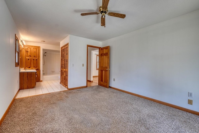 unfurnished bedroom with baseboards, ensuite bath, a closet, a textured ceiling, and light carpet