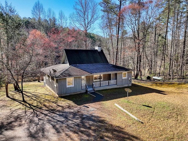 view of front facade featuring a front yard, a forest view, covered porch, and a chimney