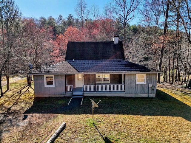 view of front of property featuring a chimney, roof with shingles, covered porch, and a front yard