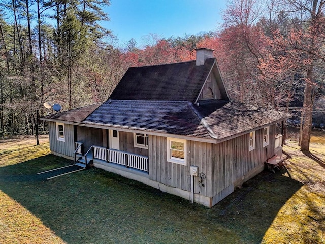 view of front of house featuring a front yard, covered porch, a chimney, and a shingled roof