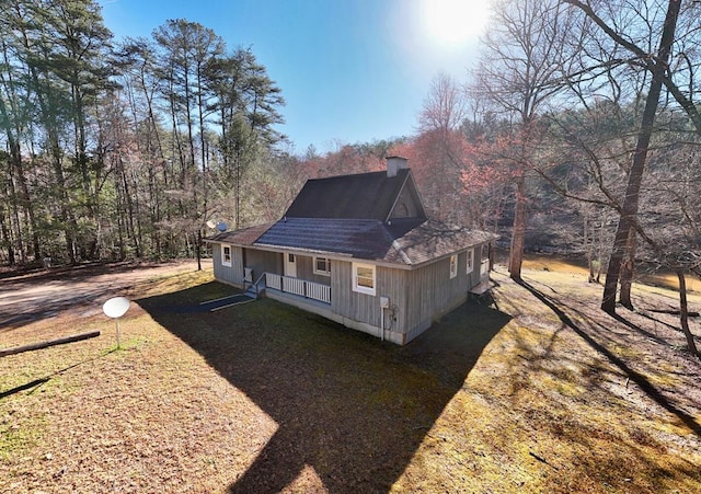 rear view of house featuring a lawn, covered porch, roof with shingles, and a chimney