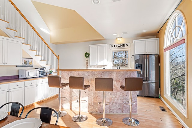 kitchen featuring stainless steel fridge with ice dispenser, white microwave, plenty of natural light, recessed lighting, and lofted ceiling