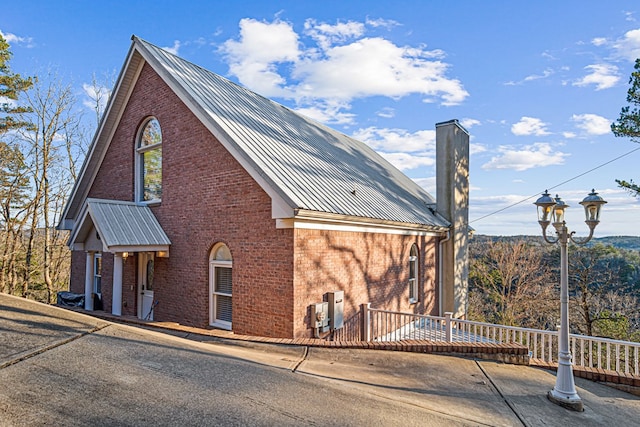 view of front facade featuring brick siding, metal roof, and a chimney