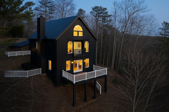 back of property featuring a chimney, board and batten siding, a balcony, and metal roof