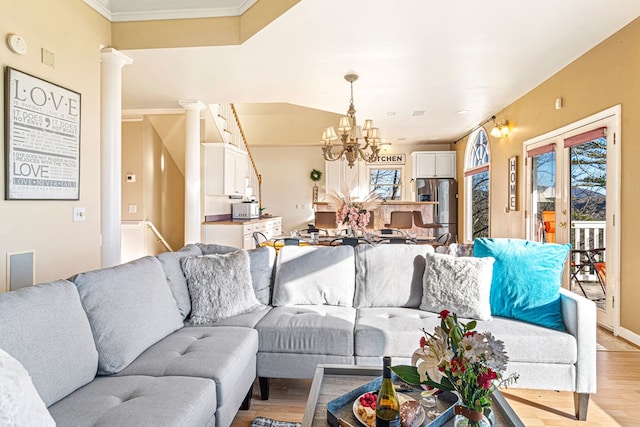 living room featuring healthy amount of natural light, light wood-style flooring, a chandelier, ornamental molding, and ornate columns