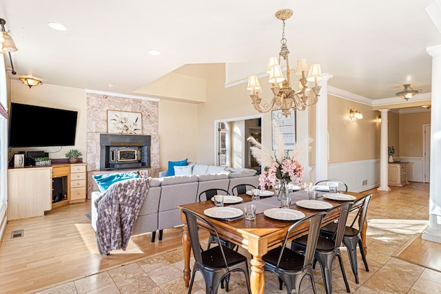 dining area with decorative columns, crown molding, a chandelier, and a tiled fireplace
