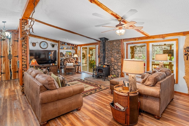 living room featuring lofted ceiling, a ceiling fan, a wood stove, a textured ceiling, and wood finished floors