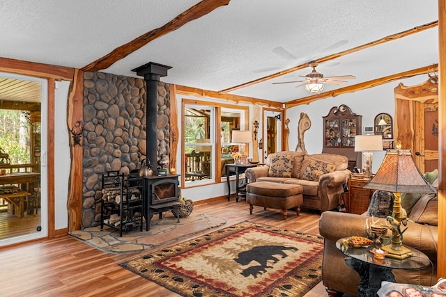 living area featuring beam ceiling, a wood stove, ceiling fan, a textured ceiling, and wood finished floors