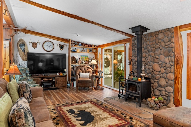 living room featuring a wood stove, vaulted ceiling with beams, a textured ceiling, and wood finished floors