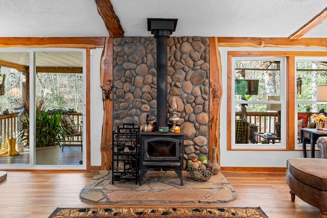 living room with a textured ceiling, wood finished floors, baseboards, beamed ceiling, and a wood stove