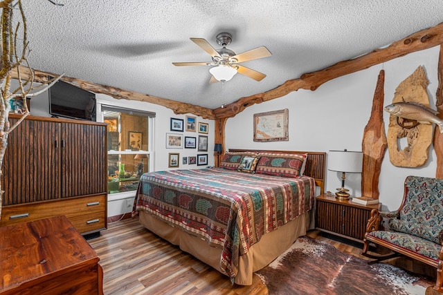 bedroom with a ceiling fan, beamed ceiling, a textured ceiling, and wood finished floors