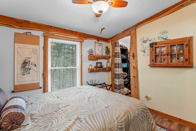 bedroom featuring a textured ceiling, ceiling fan, wood finished floors, baseboards, and a spacious closet