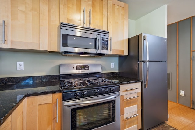 kitchen with dark stone countertops, light brown cabinetry, stainless steel appliances, and hardwood / wood-style flooring