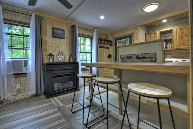 bar with wood walls, light wood finished floors, a glass covered fireplace, and ceiling fan