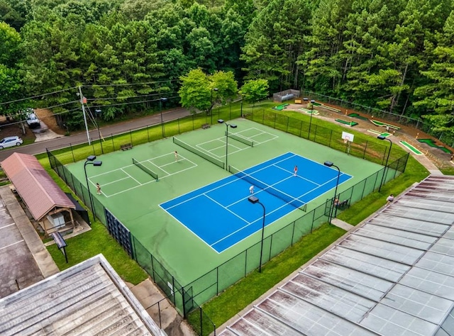 view of sport court featuring fence, a lawn, and a wooded view