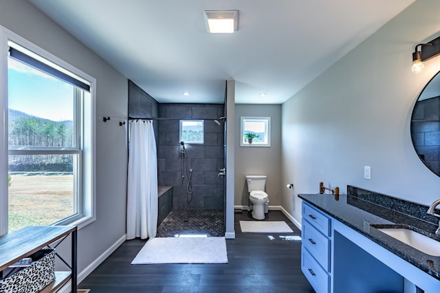 bathroom featuring toilet, vanity, wood finished floors, tiled shower, and baseboards