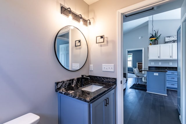 half bath with vaulted ceiling, vanity, toilet, and wood finished floors