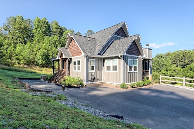 view of front of home with board and batten siding, roof with shingles, fence, and driveway