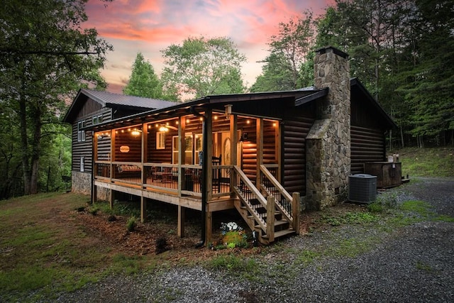 rear view of property featuring faux log siding, metal roof, central AC, and a chimney