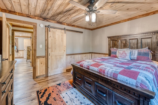 bedroom featuring wooden walls, light wood-style floors, wainscoting, a barn door, and wooden ceiling